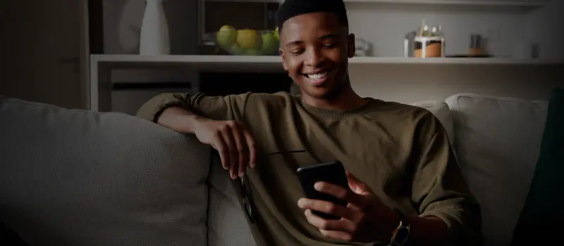 Rapaz sorrindo no sofá olhando o celular
